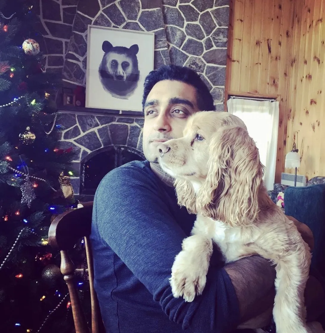 The man holding the fork, with his spaniel, beside a stone fireplace and a Christmas tree